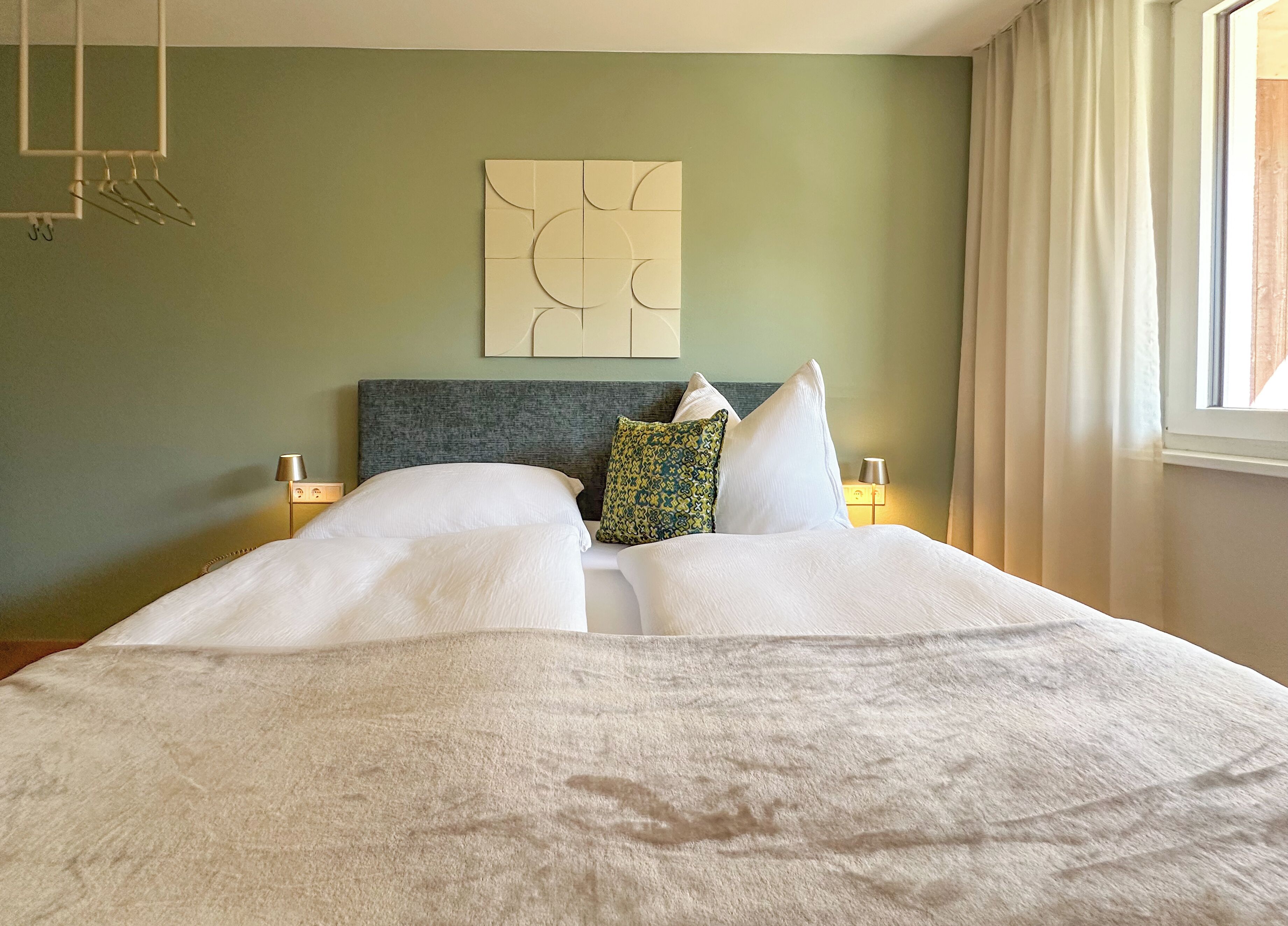 A neatly made bed with white linens, a grey headboard, and two bedside lamps.