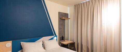 Una habitación de hotel con cama, mesita de noche, espejo y ventana con cortinas.