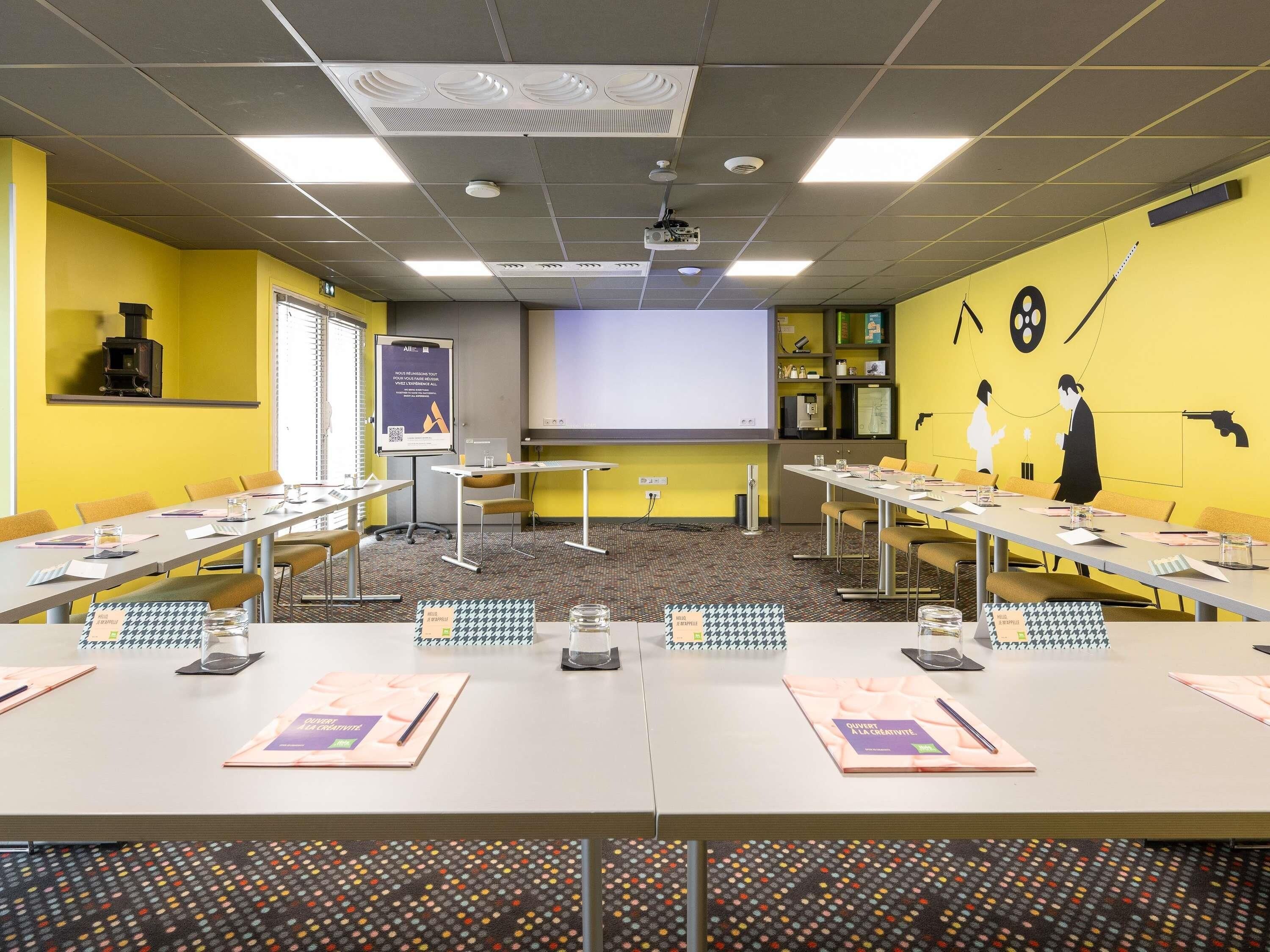 A conference room with tables, chairs, a projector screen, and a presentation board.