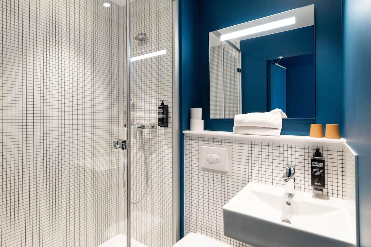 Bany modern amb boxa de dutxa de vidre, un lavabo blanc i una paret d'accent blau.