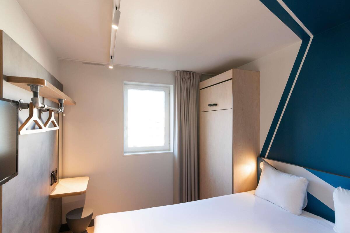 Una habitació d'hotel amb llit, finestra, armari i una taula de nit.