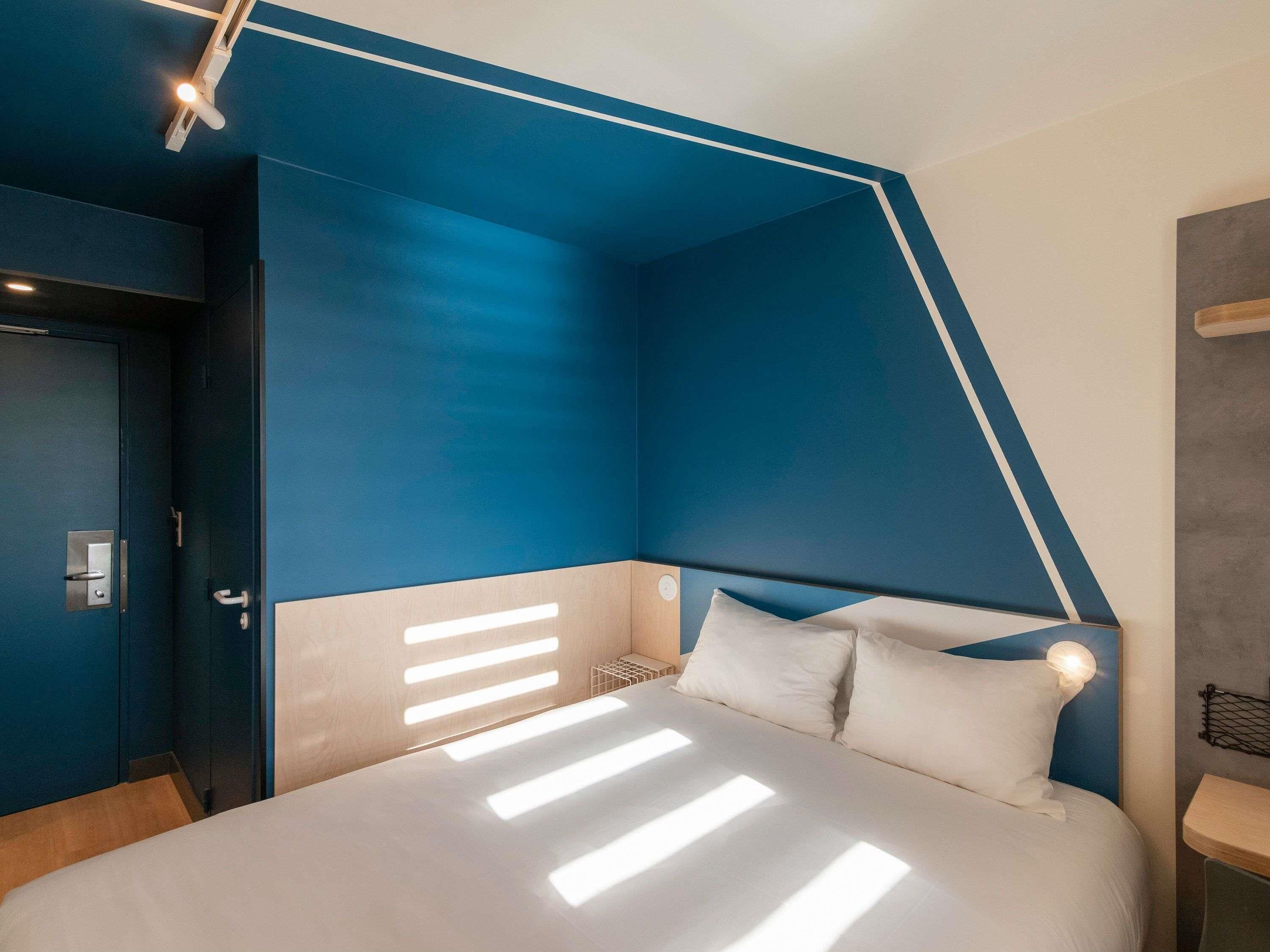 Une chambre moderne avec un plafond en pente, un lit recouvert de draps blancs et une porte dotée d’une poignée.