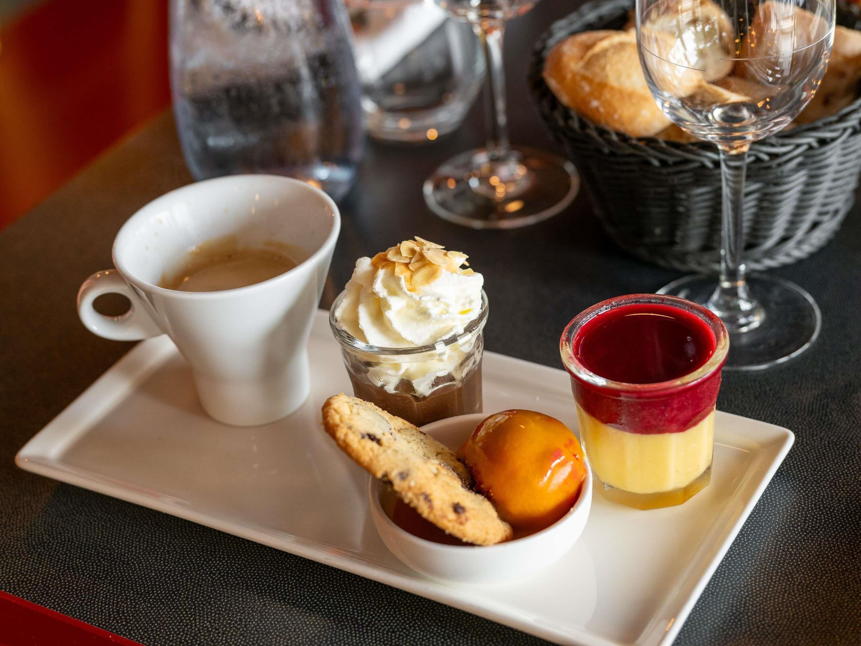 A tray with a cup of coffee, a dessert with whipped cream, a jelly dessert, and a cookie.