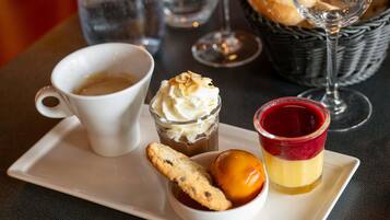A tray with a cup of coffee, a dessert with whipped cream, a jelly dessert, and a cookie.