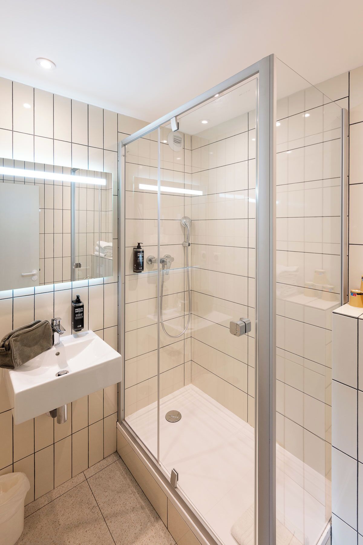 Un baño moderno con ducha de vidrio, lavamanos blanco y espejo sobre el lavamanos.