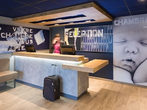 A reception desk with a suitcase, a wall with a baby image, and a sign that reads 'RECEPTION.'