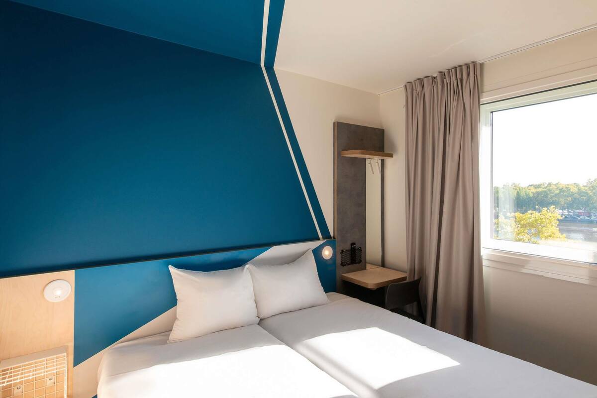 Habitació d'hotel amb llit, escriptori, mirall i finestra amb cortines.