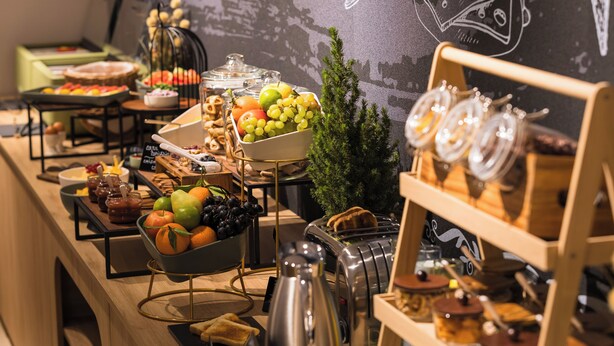 A buffet with various food items and a chalkboard wall with fruit illustrations. - Mercure Bucharest Cantemir (Bucharest)