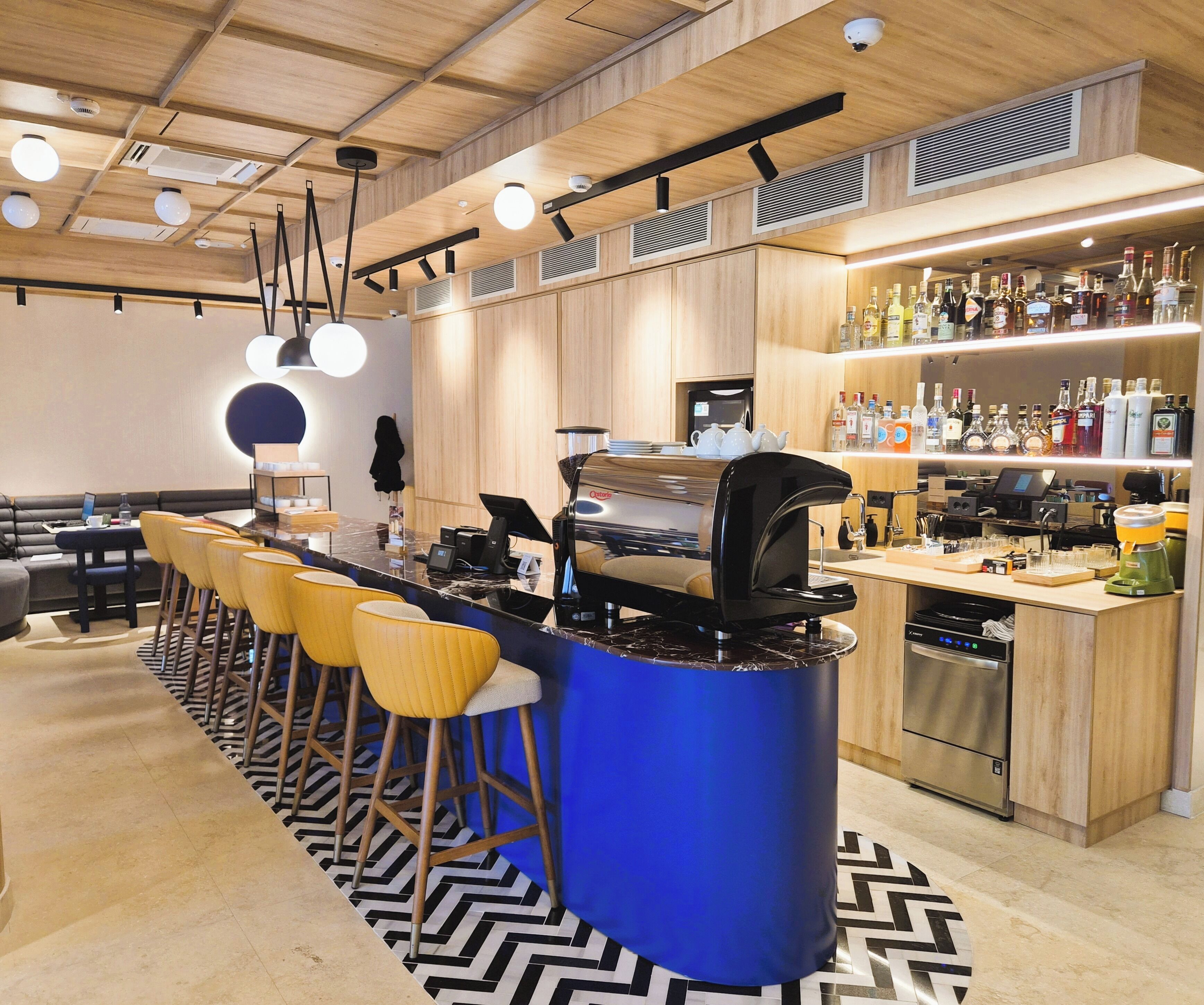A modern bar area with a blue bar counter, wooden stools, and a variety of liquor bottles.