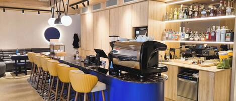 A modern bar area with a blue bar counter, wooden stools, and a variety of liquor bottles.