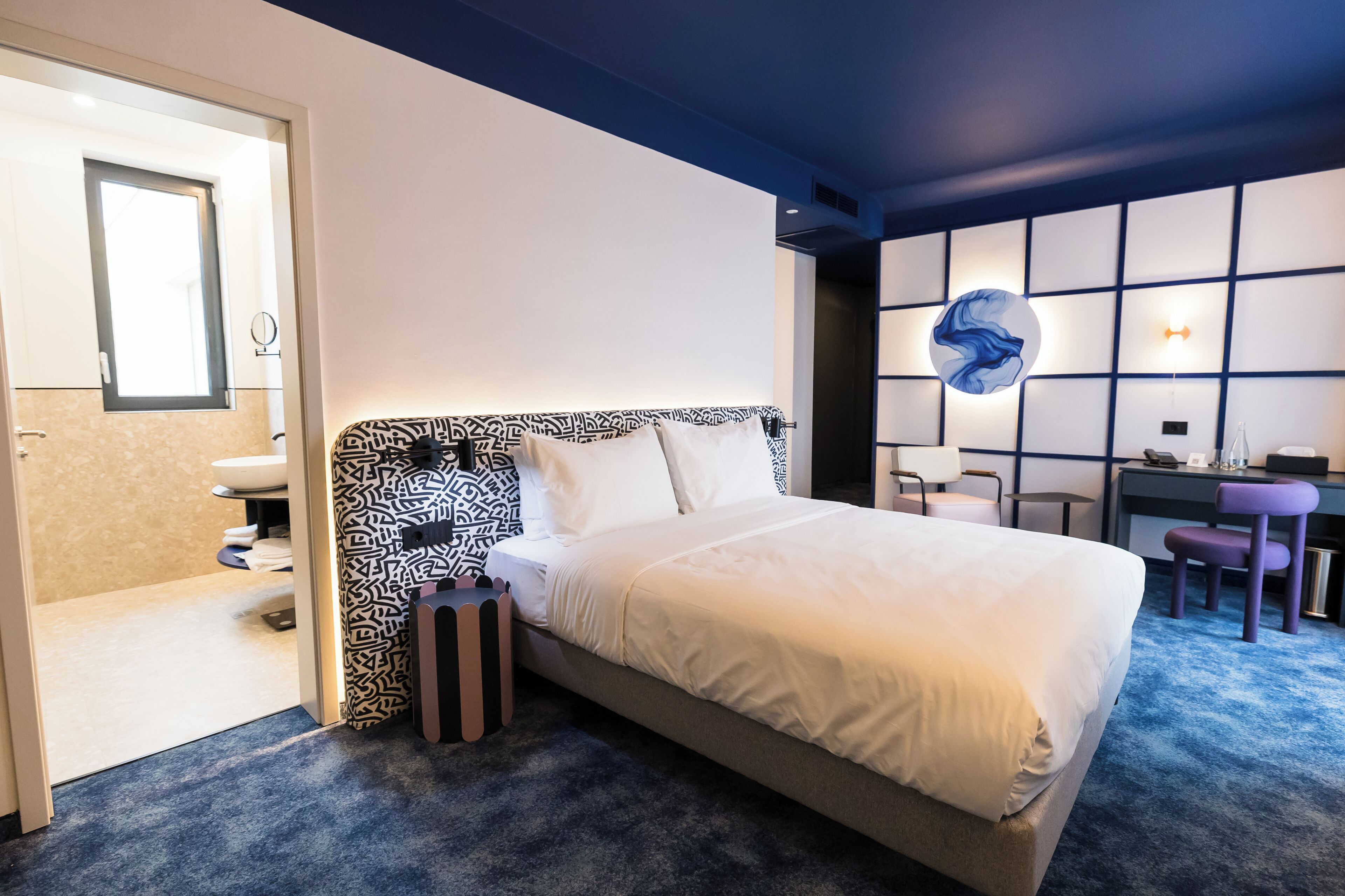 A hotel room with a bed, a desk, a chair, and a bathroom.