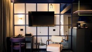A modern hotel room with a large flat-screen TV, a desk with a telephone, a chair, a small table with a glass, and a coffee maker. - Mercure Bucharest Cantemir (Bucharest)