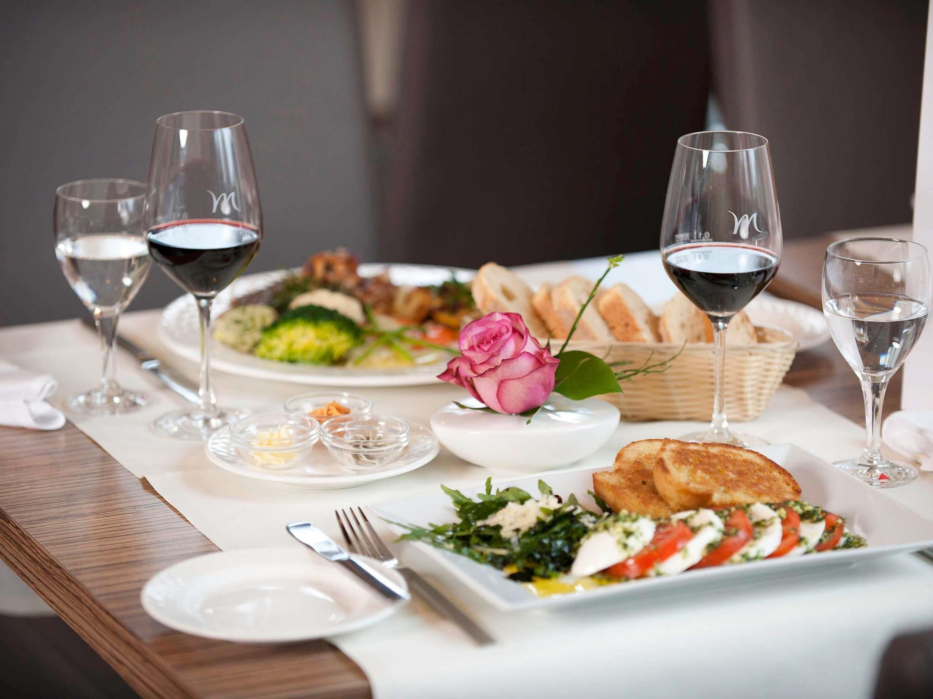 A dining table set with plates of food, wine glasses, and a rose.