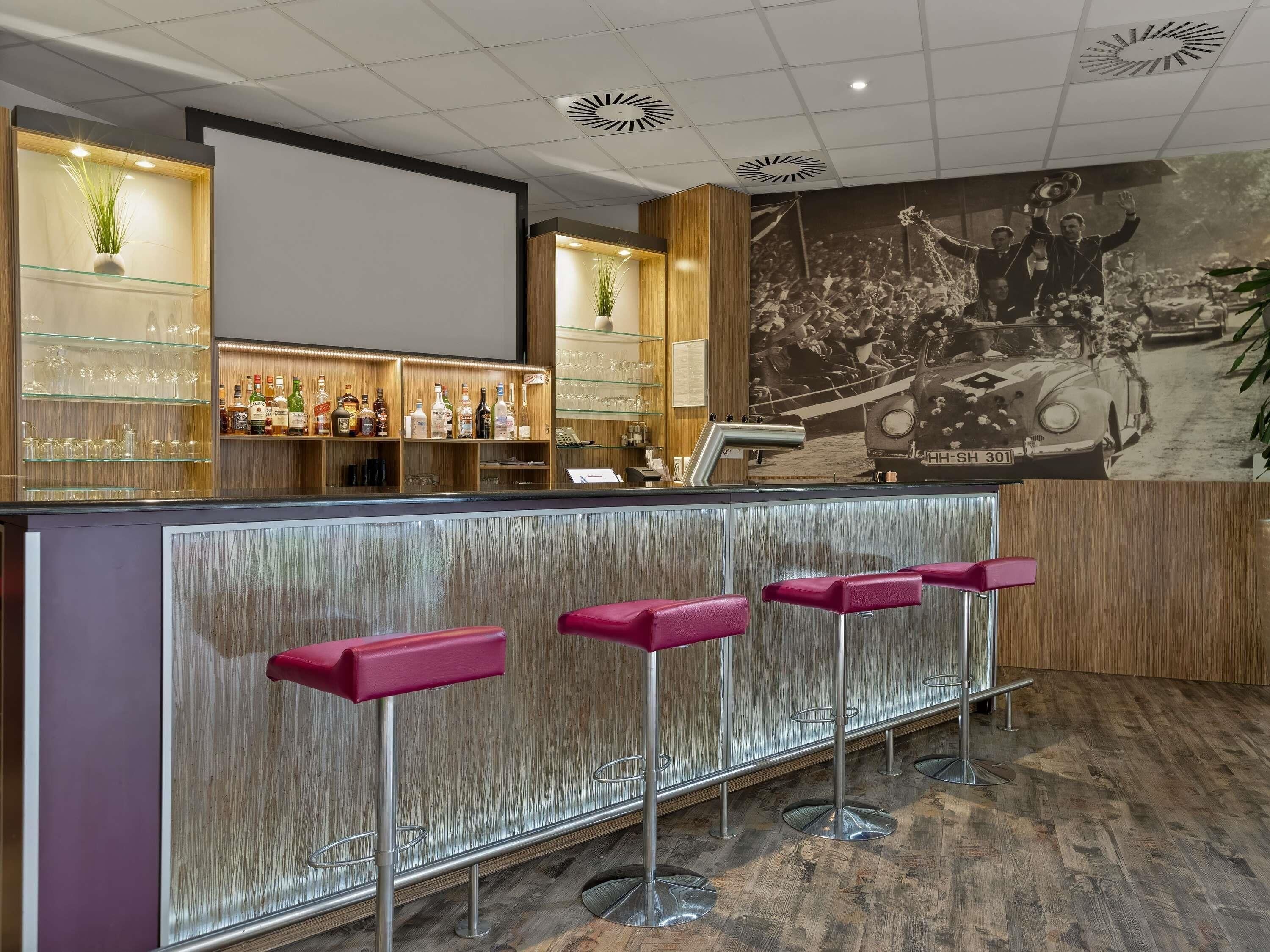 A bar area with a wooden counter, bar stools, and a wall with a vintage car photo.