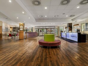 A hotel lobby with a reception desk, seating area, and a large window. - Mercure Hotel Hamburg Am Volkspark (Hamburg)