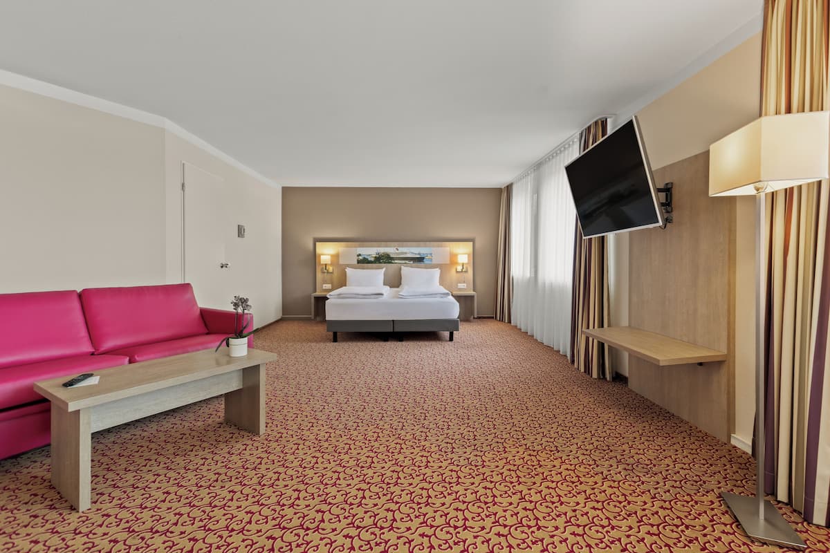 A hotel room with a bed, a pink sofa, a TV, and a patterned carpet.