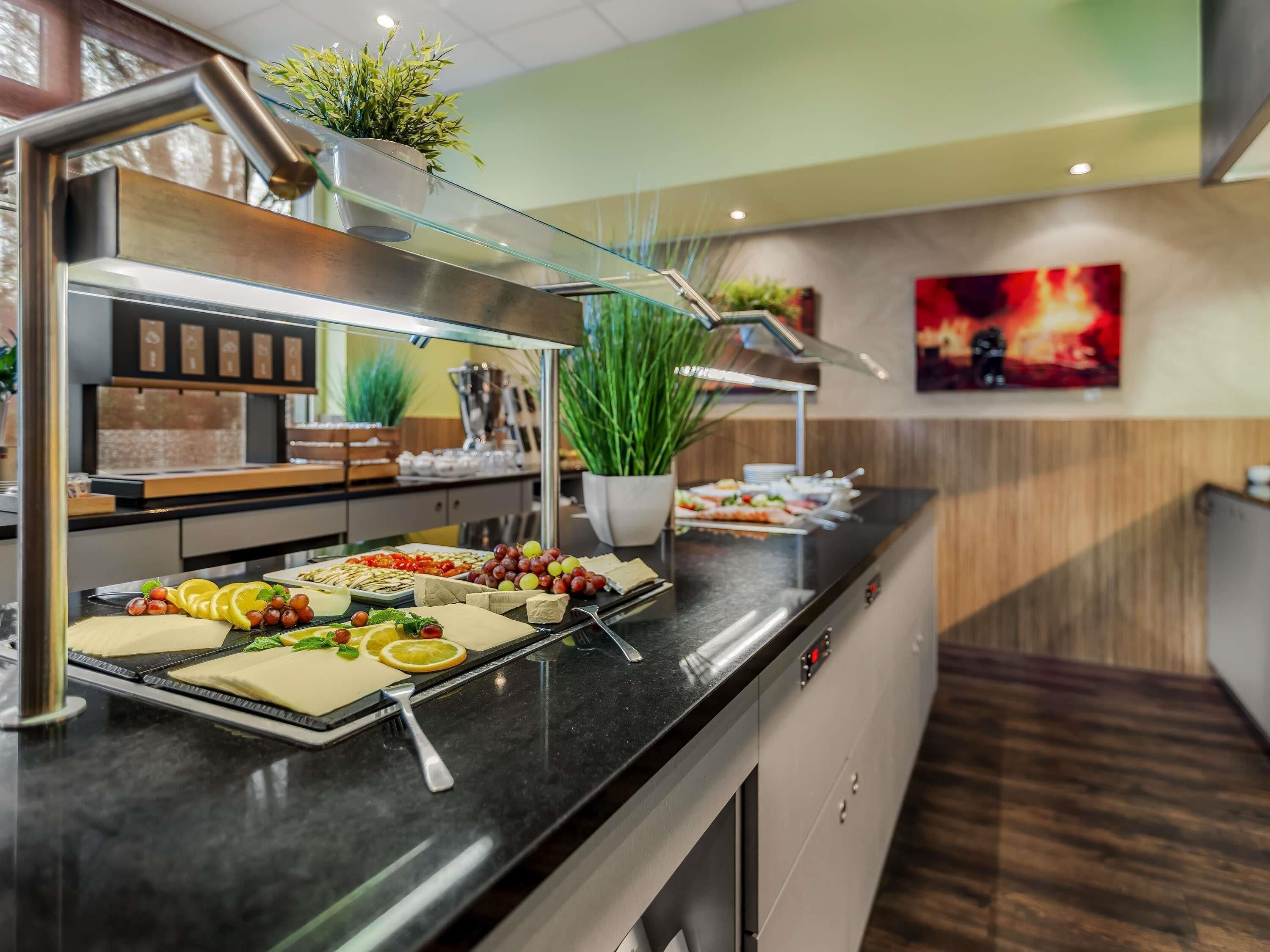 A buffet with various food items, a potted plant, and a painting on the wall.