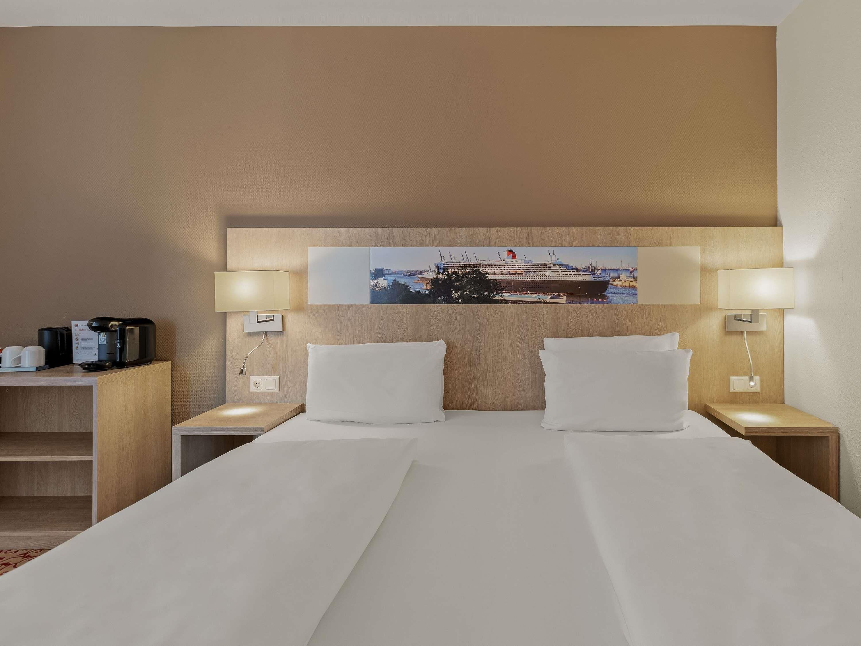 Ein Hotelzimmer mit einem großen Bett, zwei Nachttischen, einer Kaffeemaschine und einem Wandbild.