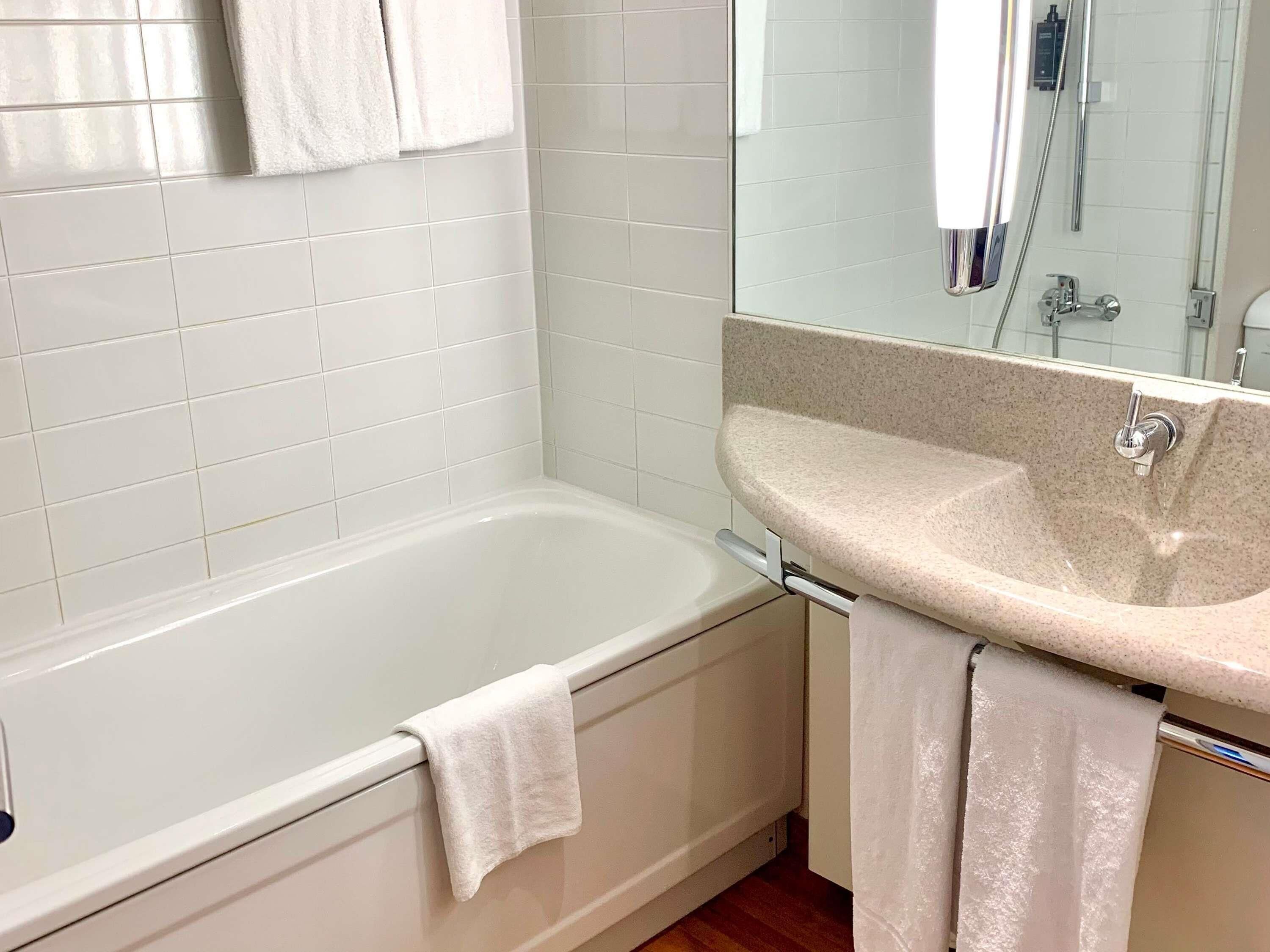 A bathroom with a white bathtub, a sink with a mirror, and a towel hanging on the wall.