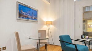 A modern room with a glass table, two chairs, a blue armchair, a floor lamp, and a digital clock. - 1-Bed Flat Sleeps 4 · Marble Bath · Walk to Monument & Bank (Greater London)