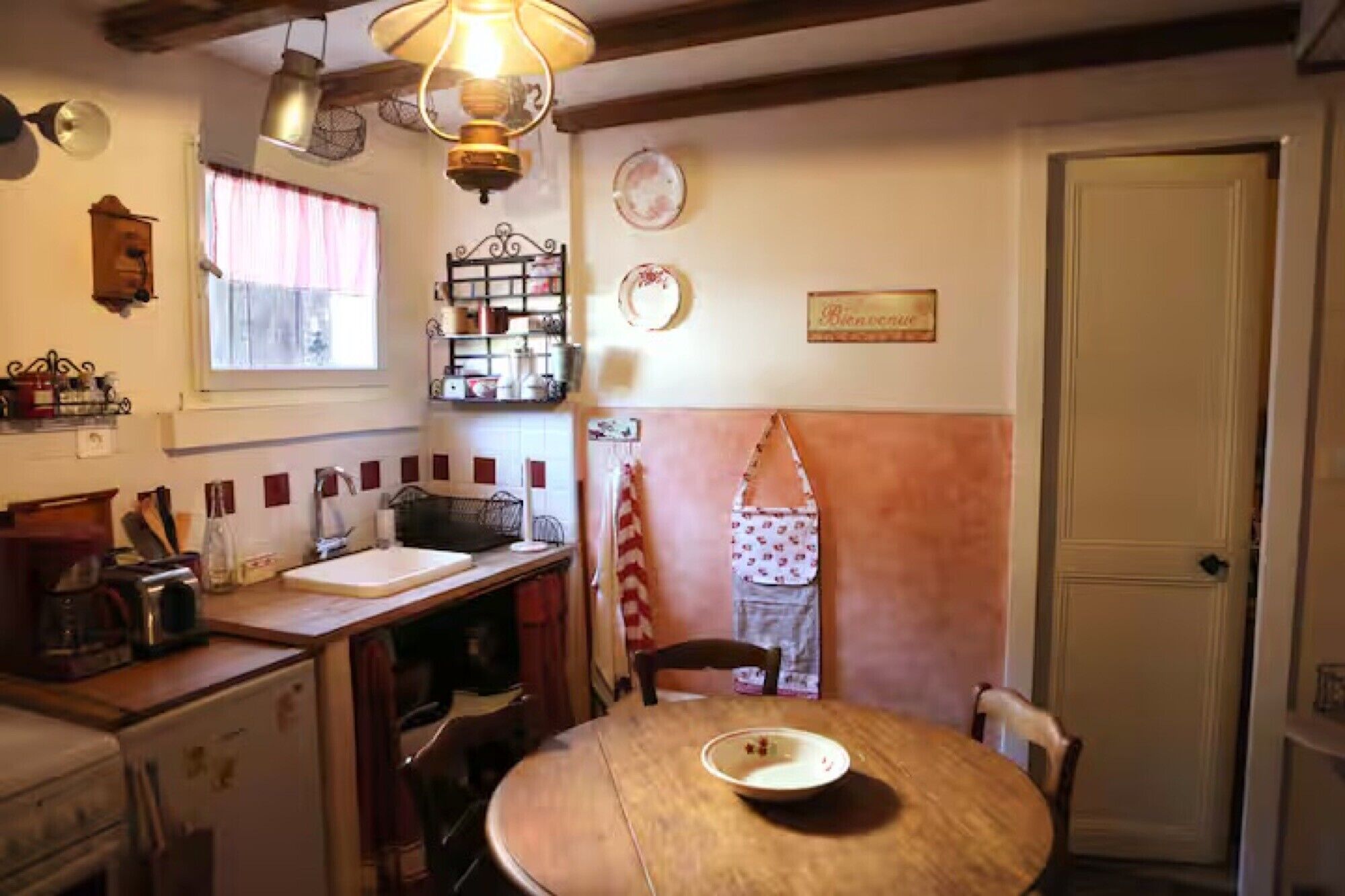 Une cuisine avec une table en bois, un évier et une fenêtre avec des rideaux.