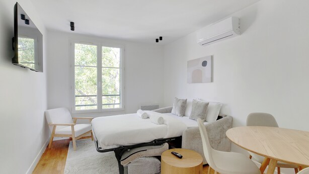 Ein modernes Schlafzimmer mit Bett, einer Couch, einem Esstisch und einem Fernseher.