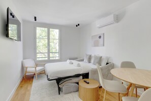 A modern bedroom with a bed, a sofa, a dining table, and a TV. - Appartements rue du Maréchal Leclerc (Saint-Ouen)