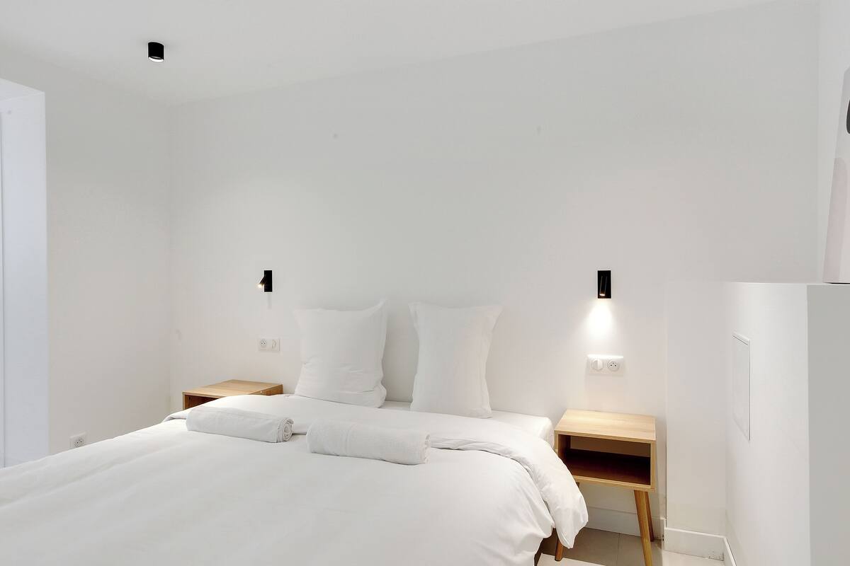 Quarto de hotel minimalista com uma cama grande, duas mesas de cabeceira e iluminação embutida na parede.