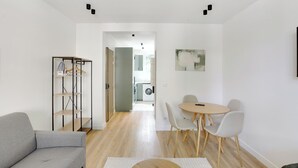 Ein modernes Wohnzimmer mit grauem Sofa, einem Esstisch mit Stühlen, Holzboden und einem Flur, der in eine Küche führt.