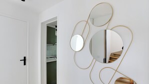 Ein Flur mit einer weißen Tür, einem Spiegel mit goldfarbenen Rahmen und einer sichtbaren Treppe durch eine offene Tür.