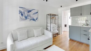 Ein modernes Wohnzimmer mit einem weißen Sofa, einem Gemälde und einer Küchenzeile mit grauen Schränken.