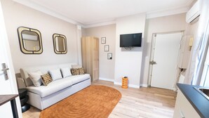 A modern living room with a sofa, a brown rug, wooden flooring, a TV mounted on the wall, and a door leading to another room. - Appartements rue de Fécamp (Paris)