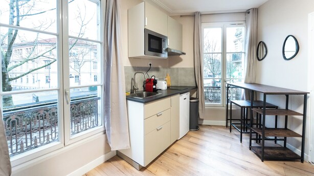 A compact kitchen with a microwave, sink, and a small dining area with a table and chairs. - Appartements rue de Fécamp (Paris)
