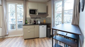 A compact kitchen with a microwave, toaster, and dishwasher. There is a dining table with benches and a window with curtains. - Appartements rue de Fécamp (Paris)