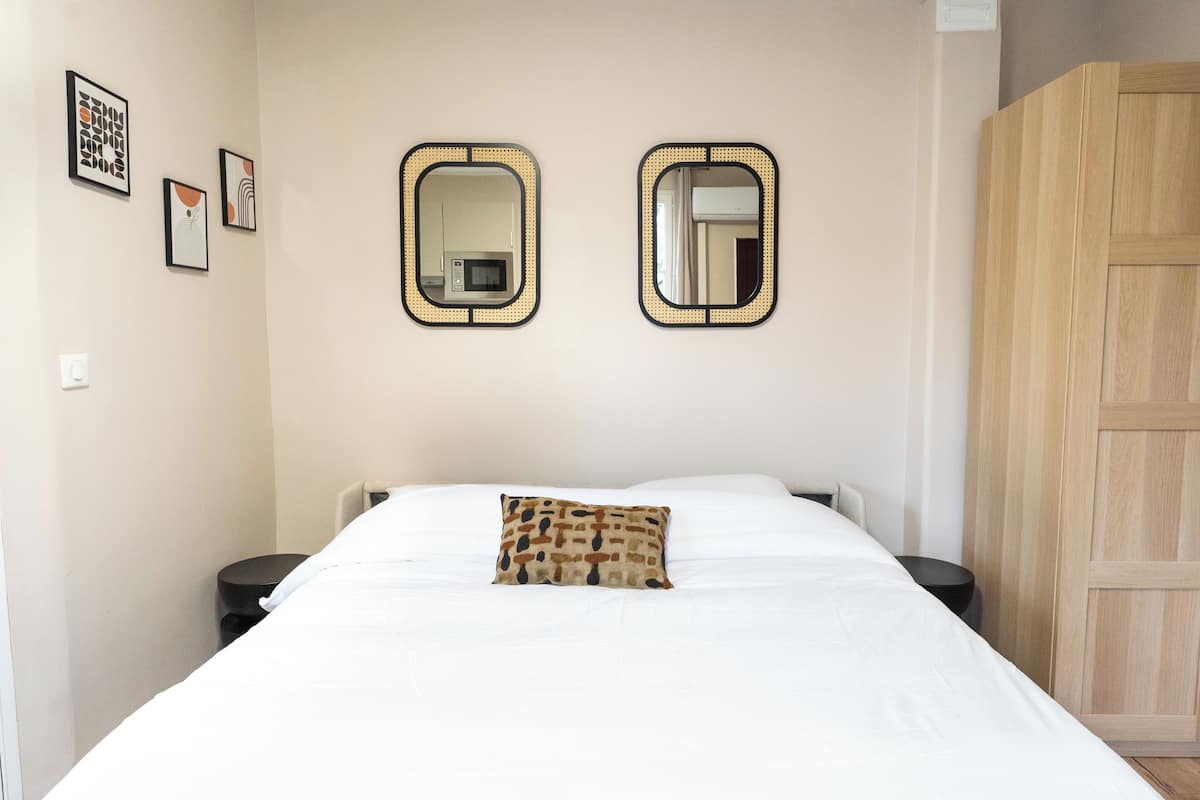 Una cama bien hecha con un cojín estampado, dos mesitas de noche y dos espejos en la pared.