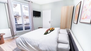 A bedroom with a bed, a television mounted on the wall, a door, and a window with curtains. - Appartements rue de Fécamp (Paris)