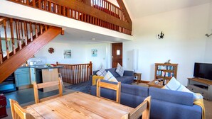 Un'ampia zona giorno con tavolo da pranzo in legno, divano blu e una scala che conduce a un piano superiore.
