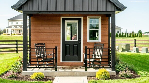 A small, single-story house with a dark roof, a front porch with two chairs, and a pathway leading to the entrance. - Natural Nook | Tiny Home #2 in Amish Country! (Shipshewana)