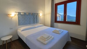 A neatly made bed with a patterned headboard, two bedside lamps, and a window with a view of the outdoors. - Cozy apartment surrounded by nature, with terrace and veranda (Palmadula)