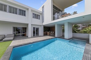 Ein modernes, zweistöckiges Haus mit Swimmingpool, Sitzgelegenheit im Freien und einem Balkon mit Blick.