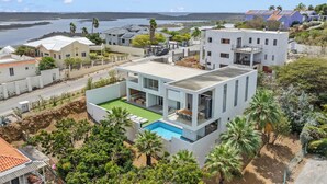 Ein modernes Haus mit Swimmingpool, umgeben von üppiger Vegetation und Blick aufs Meer.