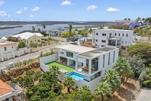 Ein modernes Haus mit Swimmingpool, umgeben von üppiger Vegetation und Blick aufs Meer.