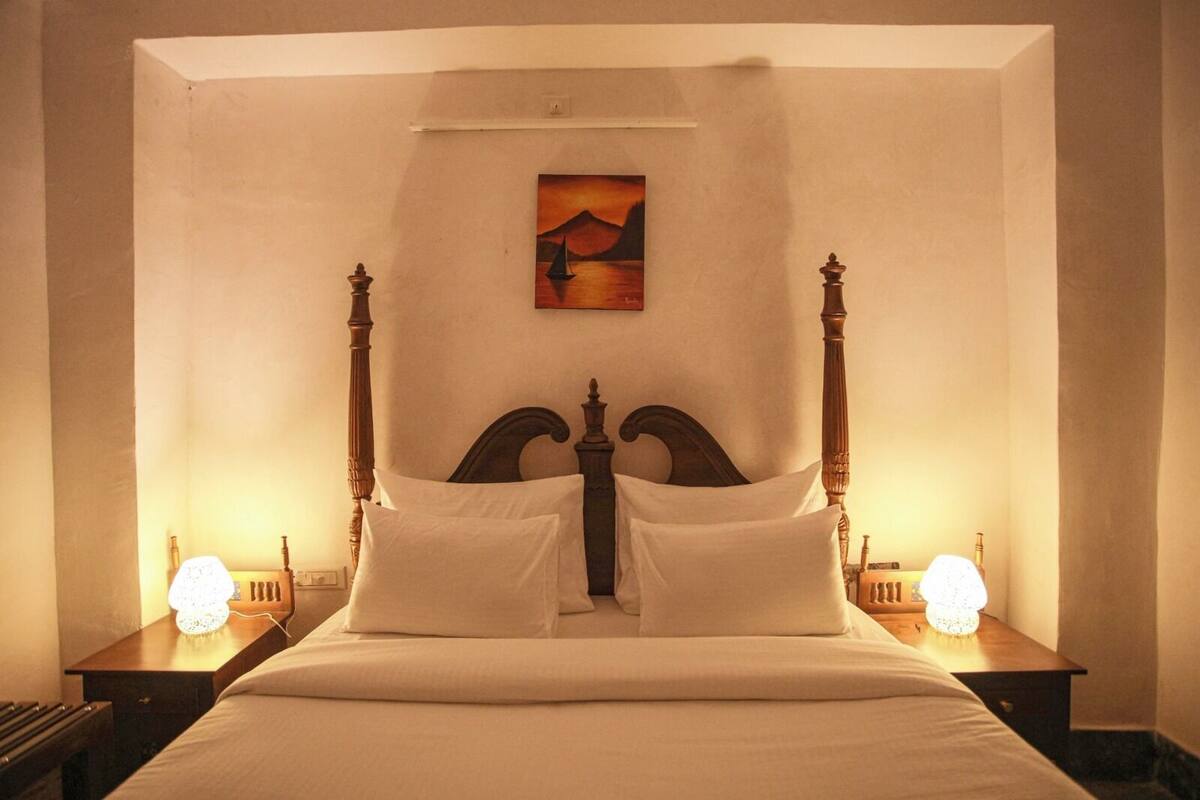 A large bed with a wooden headboard, two bedside tables with lamps, and a painting above the bed.