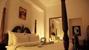 A four-poster bed with white linens, a large mirror, and a painting on the wall. - Prem Niwas 300-year-old Heritage Boutique Haveli (Udaipur)