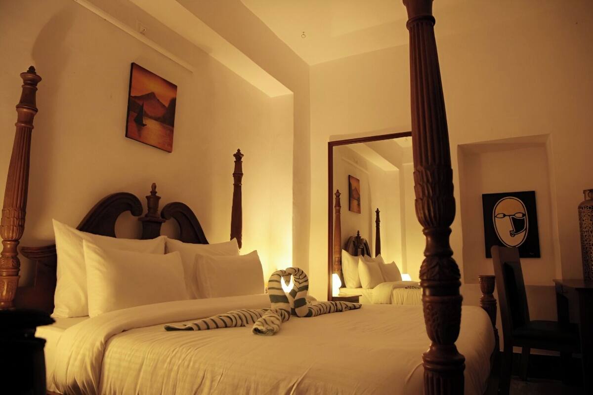 A four-poster bed with white linens, a large mirror, and a painting on the wall.