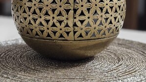 A decorative brass globe with intricate cut-out patterns, placed on a woven placemat. - Prem Niwas 300-year-old Heritage Boutique Haveli (Udaipur)