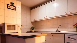 Una cocina moderna con armarios blancos, microondas, lavaplatos y una pequeña zona de comedor con una silla.