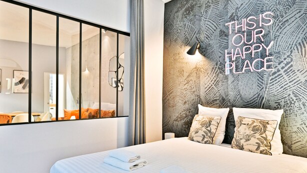 A modern hotel room with a large bed, a mirror, and a wall with a motivational quote. - Appartements rue des Jeuneurs (Paris)