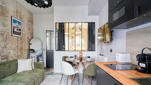 A modern kitchen with a dining area, featuring a green sofa, white chairs, and a wooden countertop with a coffee machine. - Appartements rue des Jeuneurs (Paris)