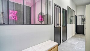 A hallway with a bench, glass doors, and a neon sign. - Appartements rue des Jeuneurs (Paris)